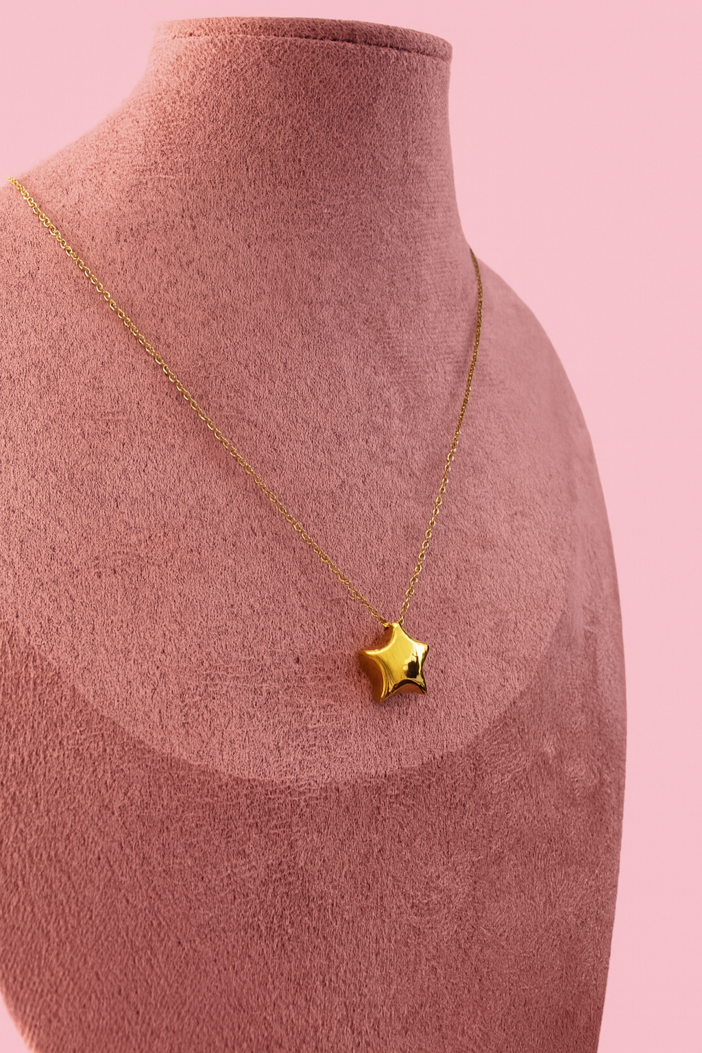 Gold star necklace on a mannequin bust against a pink background